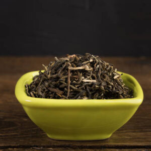 Dry green tea in a clay bowl isolated on wooden table on black background