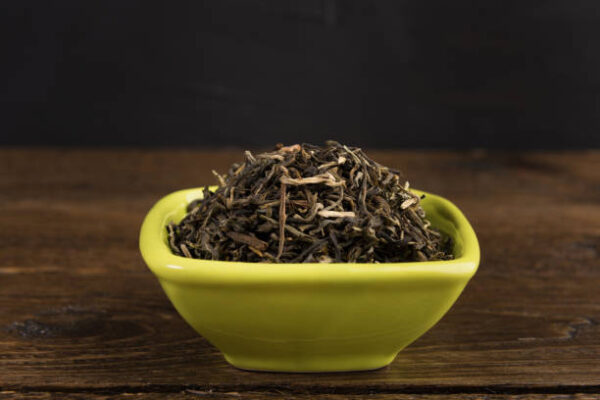 Dry green tea in a clay bowl isolated on wooden table on black background